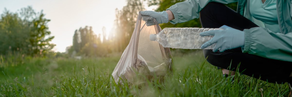 The girl collects trash from the forest in the trash bag Eine Plastikflasche wird in einen Müllbeutel gesteckt.