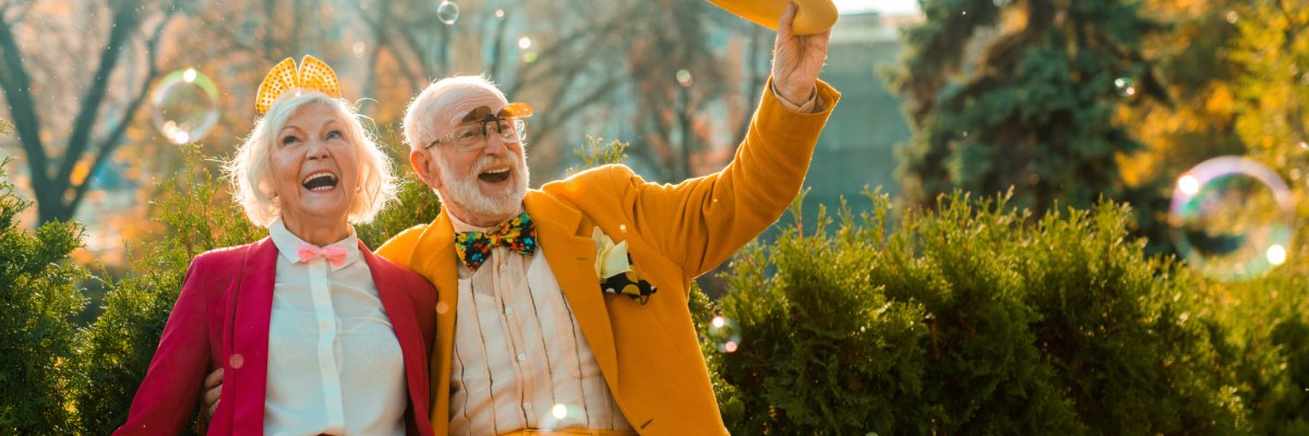 Glückliches Seniorenpaar, bunt gekleidet. Sie genießen die Zeit und lächeln tanzend in die Kamera.