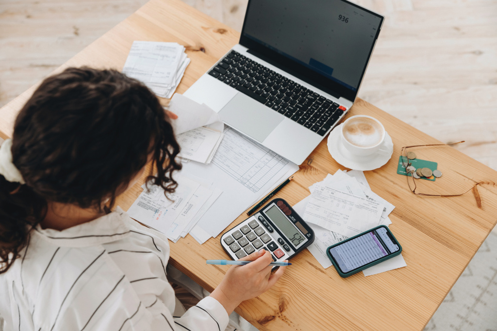 Top view of a woman working at home in the kitchen with financial papers, counting on a calculator, paying bills, planning a budget to save some money. Independent accounting, remote accountant Frau sitzt am Laptop.