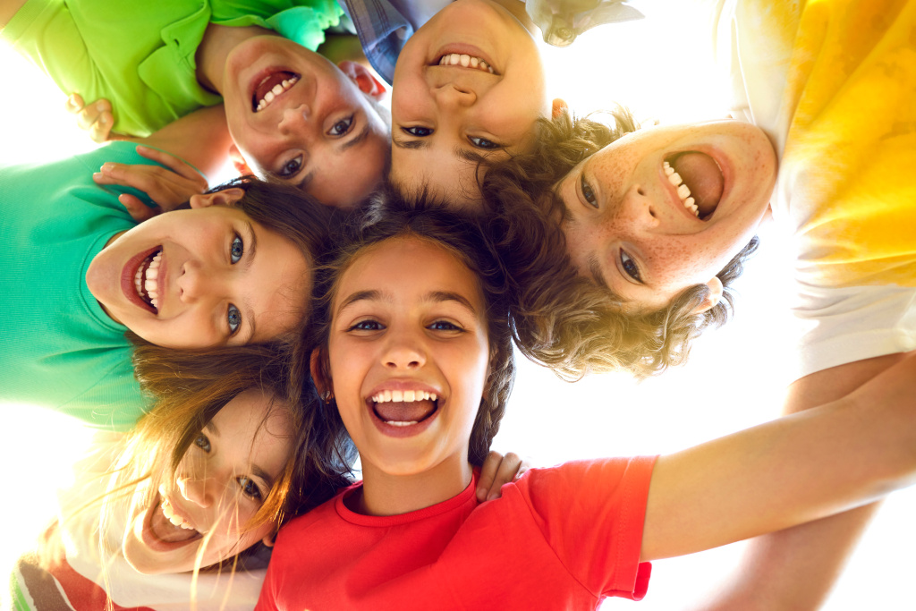 Group of happy little children playing together, having fun, huddling, looking down and smiling Mehrere Kinder umarmen sich und lächeln in die Kamera