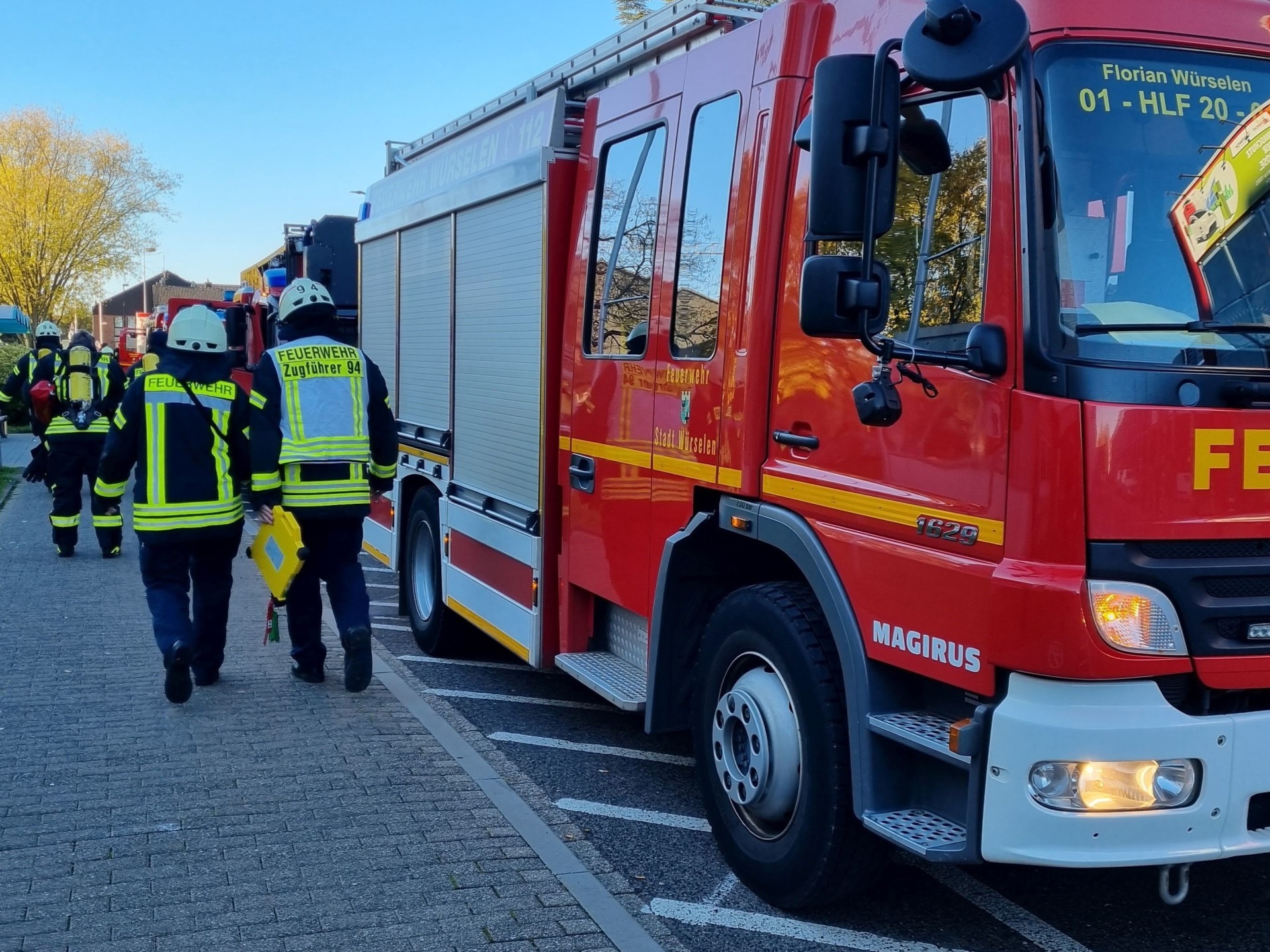 Feuerwehr Würselen Ein Feuerwehrauto am Straßenrand und Feuerwehrleute, die von hinten zu sehen sind.
