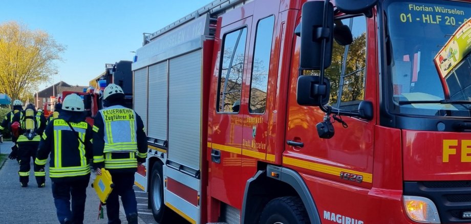 Ein Feuerwehrauto am Straßenrand und Feuerwehrleute, die von hinten zu sehen sind.