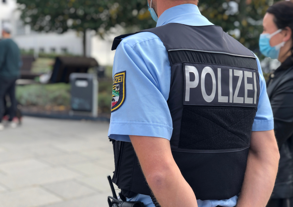 Ein Polizist von hinten, man sieht die Polizei-Jacke, er verschränkt die Arme