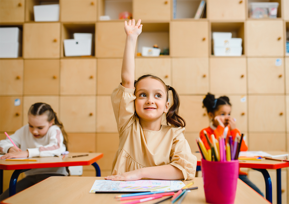 Schüler Ein Mädchen sitzt auf der Schulbank und meldet sich lächelnd.