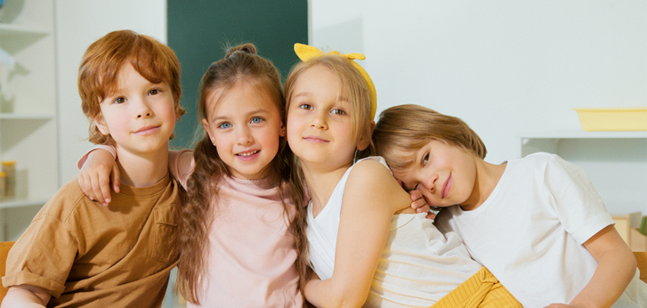 Vier kinder umarmen sich und schauen dabei in die Kamera.