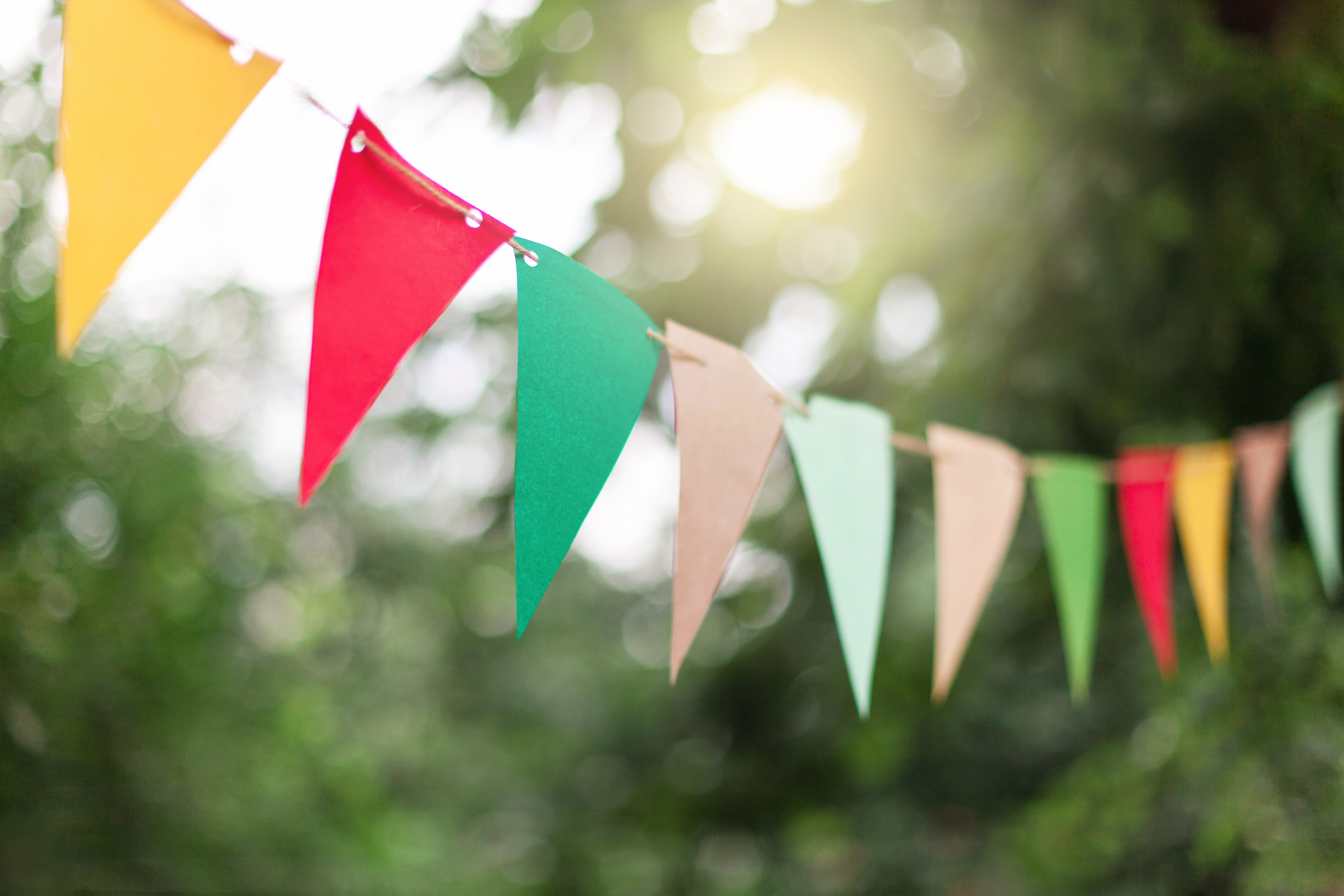 Garland of colorful flags at sunset in summer garden. Concept of celebration Happy Birthday party. Paper festive decoration outdoor.