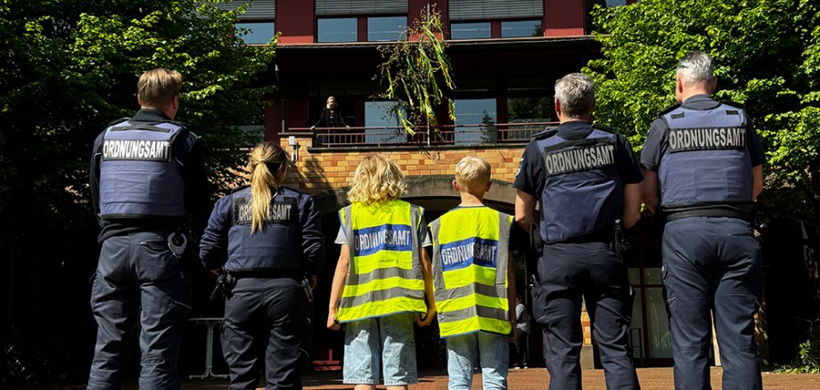 Mitarbeiter vom Jugendamt und Kinder in Warnesten stehen vor dem Rathaus. Betrachter sieht nur den Rücken der Personen.