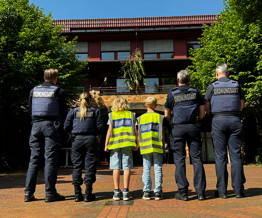 Mitarbeiter vom Jugendamt und Kinder in Warnesten stehen vor dem Rathaus. Betrachter sieht nur den Rücken der Personen.