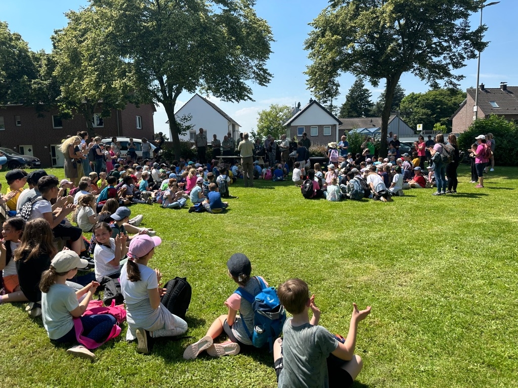 Viele Kinder sitzen auf einer Wiese im Kreis.