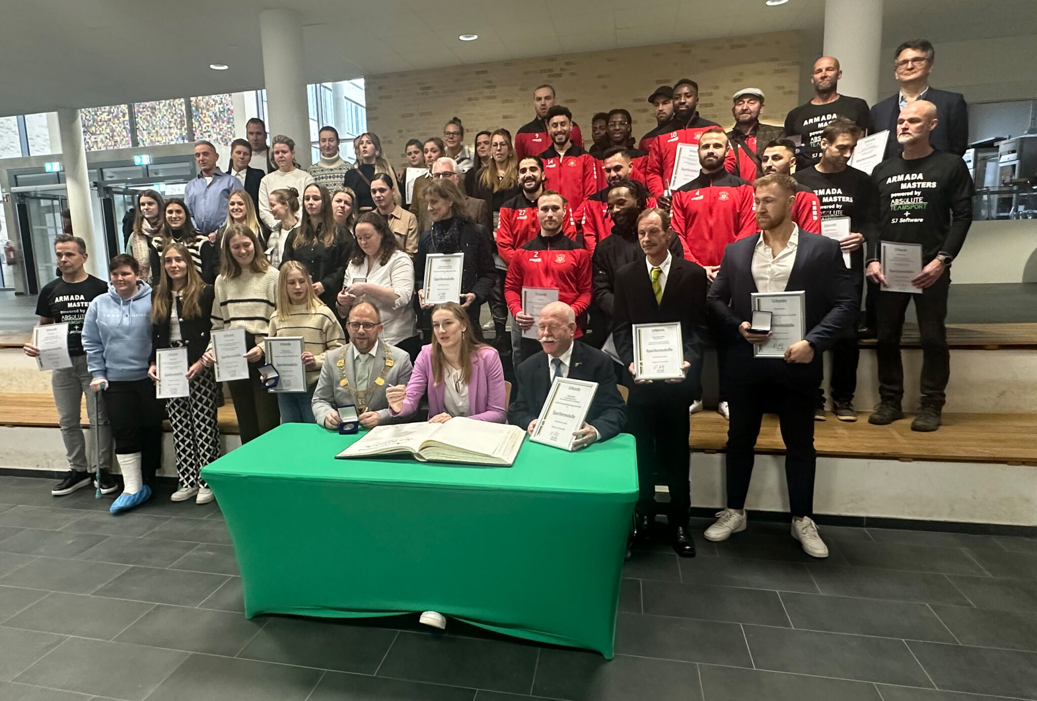 Viele Sportler hinter einem Tisch mit dem Goldenen Buch Stadt Würselen und Bürgermeister Nießen