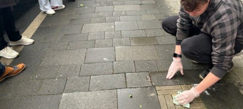 Ein junger Mann säubert einen im Boden verlegten Stolperstein mit einem Tuch.