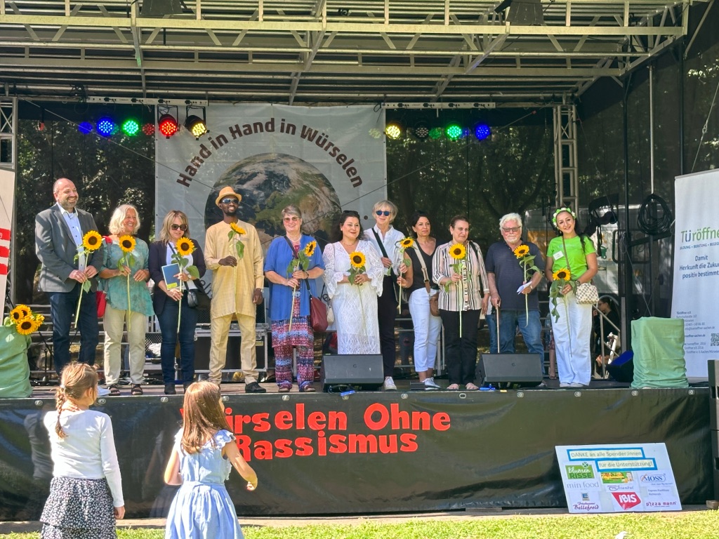 Bühne mit vielen Menschen, die eine Sonnenblume halten.