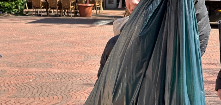 Kind hält gefüllten Müllsack in die Kamera.
