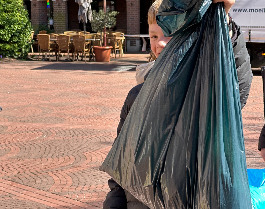 Kind hält gefüllten Müllsack in die Kamera.