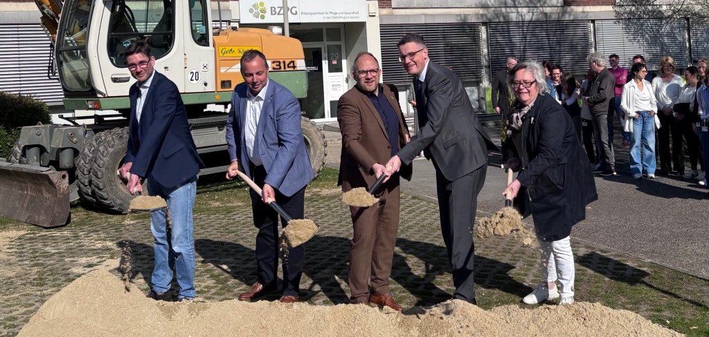 Einige Leute symbolisieren den ersten Spatenstich mit Schaufeln und Sand.