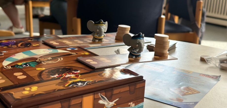 Brettspiel im Vordergrund, dahinter spielende Familien.