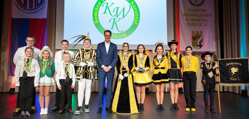 Ein Mann und zahlreiche Kinder in Karnevalsuniformen auf einer Bühne