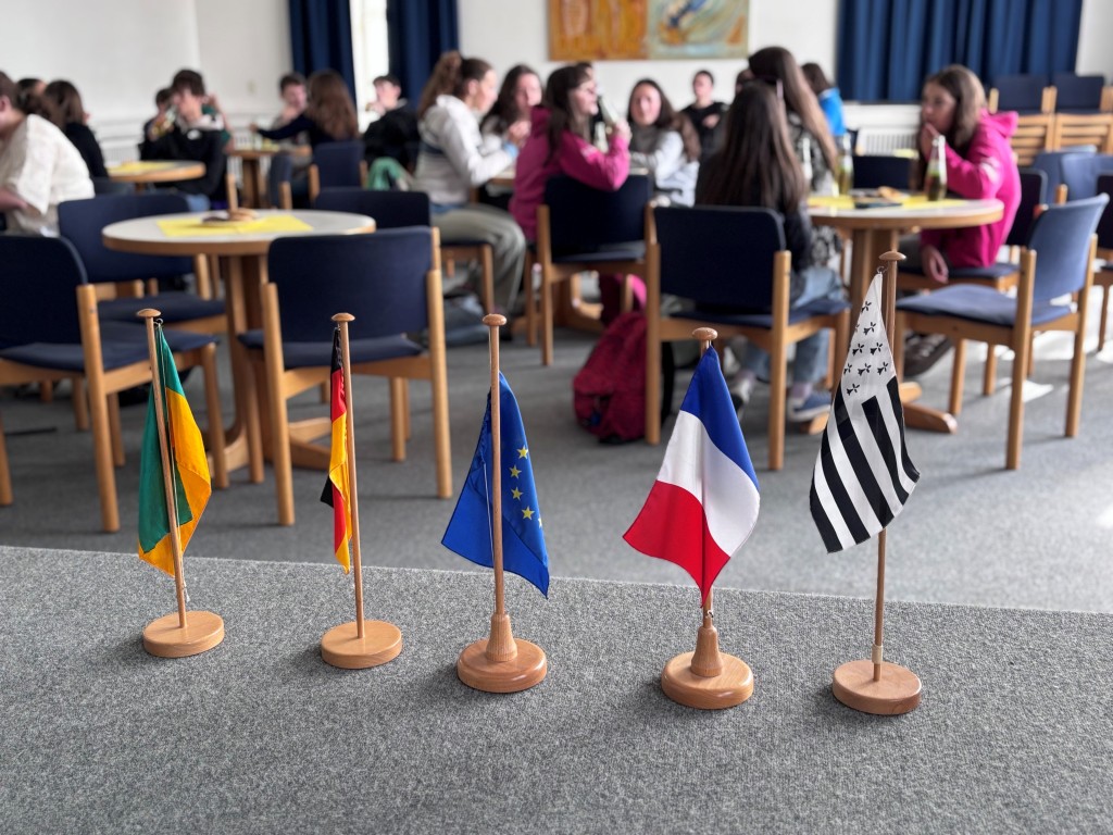 Französische Schüler im Alten Rathaus (Fahnen) Fünf Fahnen stehen auf einer Bühne, dahinter Schüler an Tischen