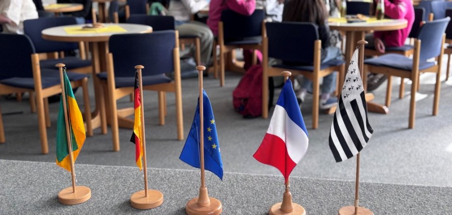 Fünf Fahnen stehen auf einer Bühne, dahinter  Schüler an Tischen