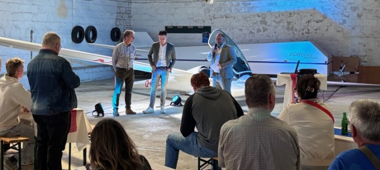 Diabolus Gäste Menschen sitzen in einem Hangar und schauen auf ein Flugzeug
