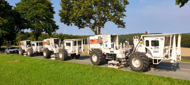 Mehrere Vibrotrucks hintereinander auf einer Straße an einer Wiese