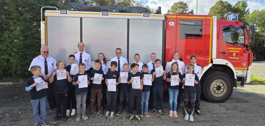 Einige Kinder vor einem Feuerwehrauto zeigen ihre Urkunden, dabei sind Erwachsene.