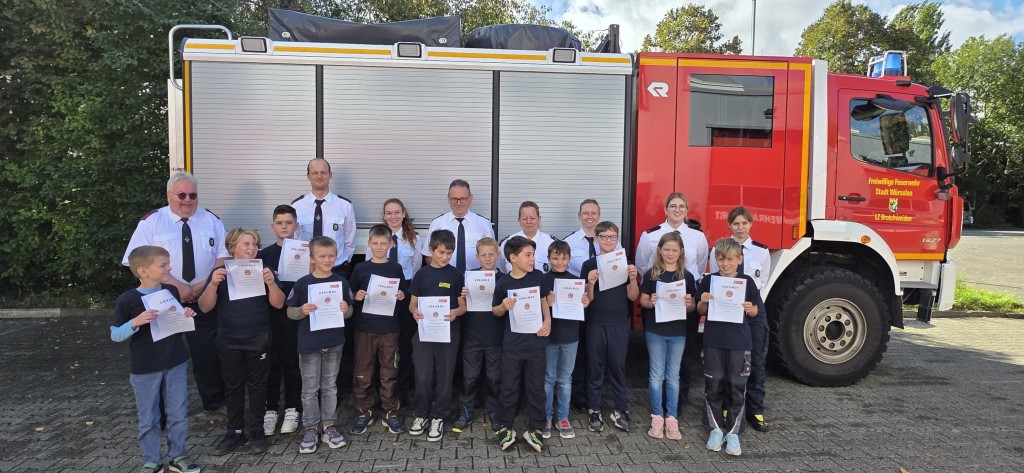 Einige Kinder vor einem Feuerwehrauto zeigen ihre Urkunden, dabei sind Erwachsene.