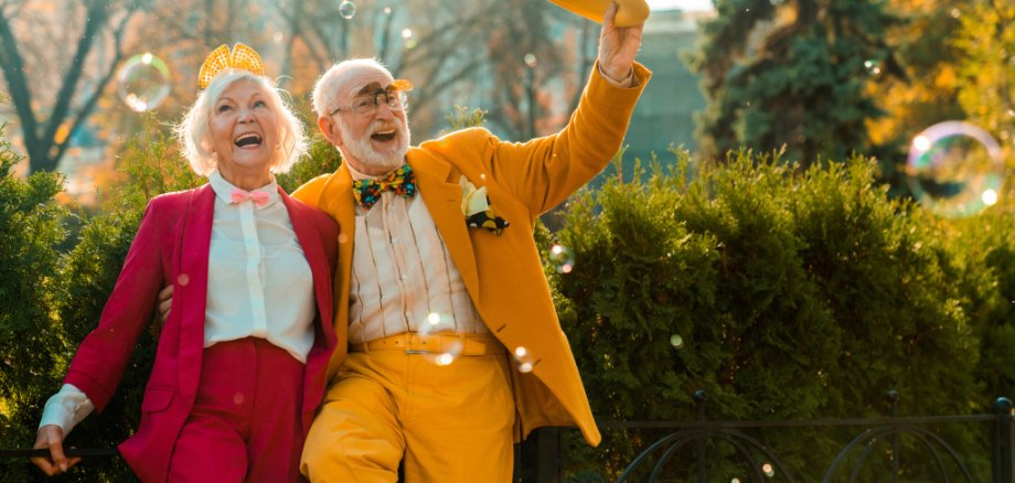 Ein glückliches älteres Pärchen in bunten Kostümen tanzt fröhlich im freien.