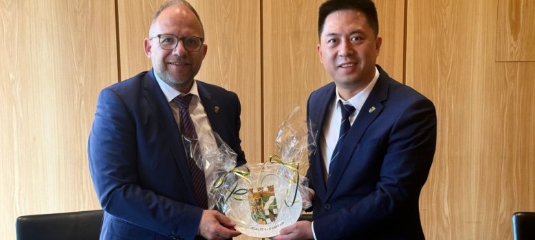 Bürgermeister Roger Nießen überreicht einen Teller mit dem Stadt Wappen der Stadt Würselen an seinen Amtskollegen WU Song