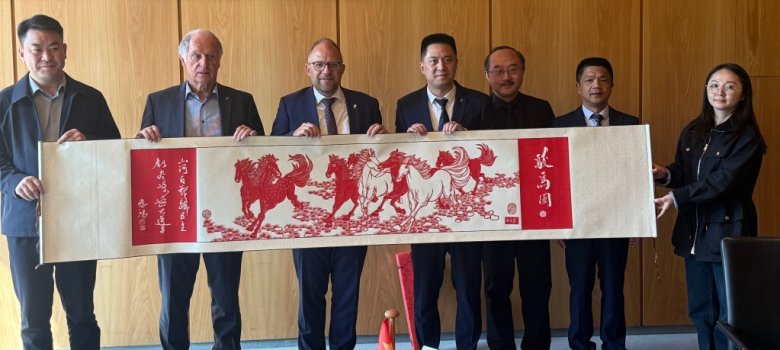 Bürgermeister Roger Nießen mit der Chinesichen delegation und dem Gastgeschenk der chinesischen Delegation: Eine kunstvolle Schrift-Bildrolle mit dem Namen "Herd of Noble Horses"