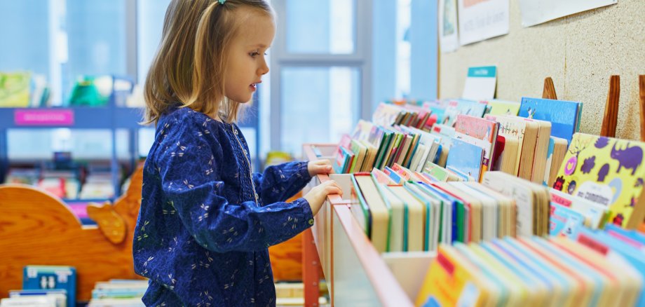 4 year old girl selecting a book in municipal library. Reading and learning concept
