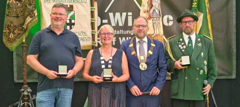 (v.l.): Dirk Nehr, Dagmar Thorand, Bürgermeister Roger Nießen, und Bezirksbundesmeister Stefan Reim Dirk Nehr, Dagmar Thorand, Bürgermeister Roger Nießen, und Bezirksbundesmeister Stefan Reim stehen gemeinsam auf der Bühne mit der Jubiläumsmedaille.