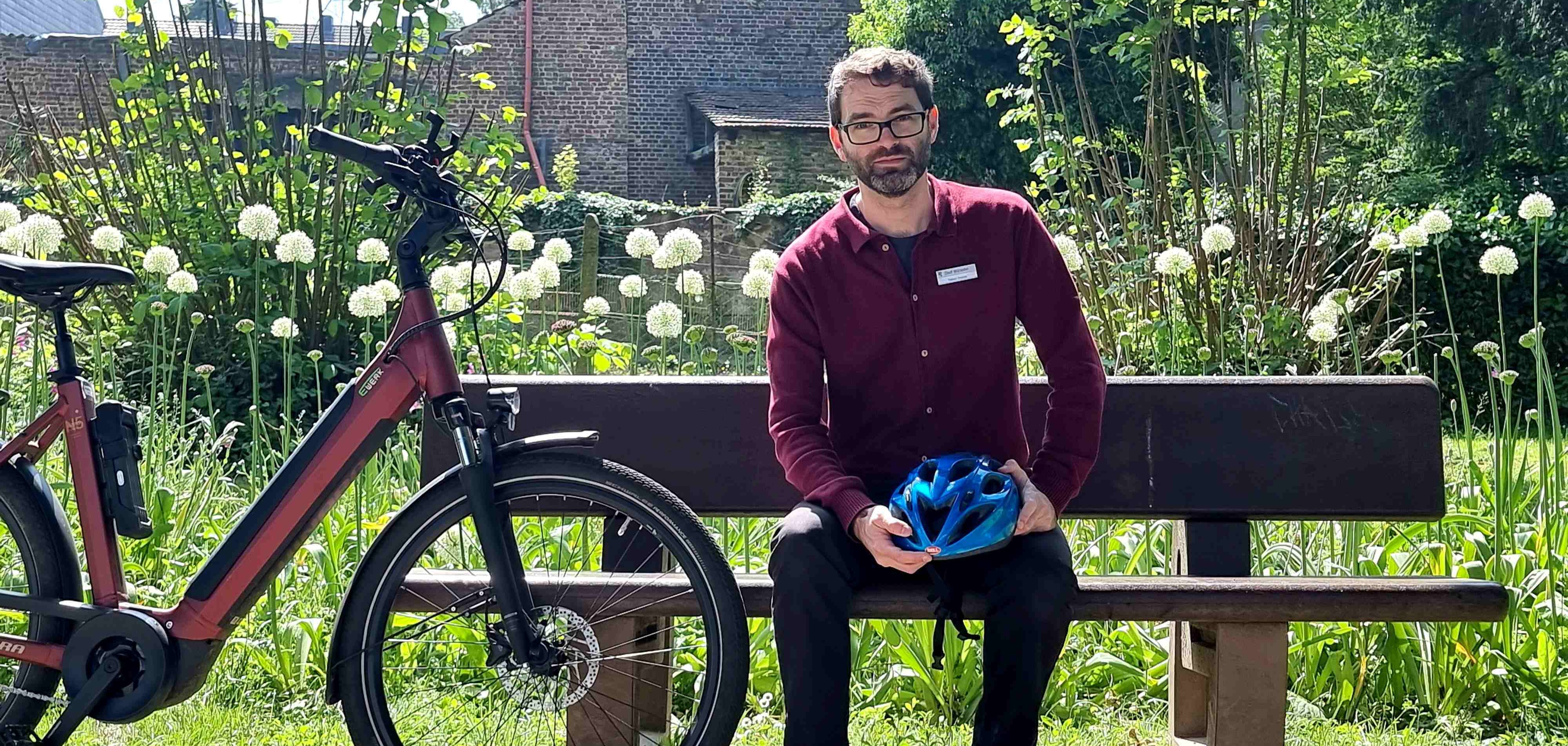 Stadtradeln 2026: Würselen knackt alle Rekorde Ein Mann mittleren Alters mit Brille sitzt auf einer Bank. Neben ihm steht ein E-Bike.